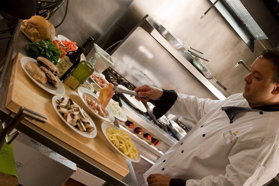 Chef in a white coat cooking over a stove with ingredients prepared on plates nearby.