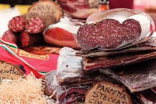Close-up of various cured meats, including salami, prosciutto, and pancetta, at a market stall.