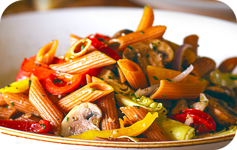Pasta salad with penne, red and yellow peppers, mushrooms, and artichoke hearts in a white bowl.