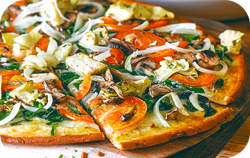 Vegetable pizza on a wooden board, sliced and topped with spinach, tomatoes, artichoke hearts, onions, and mushrooms.