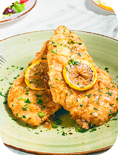 Sautéed chicken breasts in lemon butter sauce, garnished with parsley and lemon slices, on a light green plate.