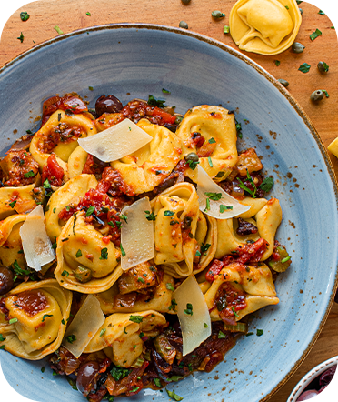 Tortellini pasta with tomato sauce, olives, and parmesan in a blue bowl, on a wooden surface.