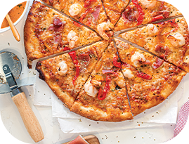 Sliced pizza with shrimp and red peppers, next to a pizza cutter and dipping sauce.