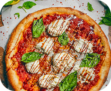 Pizza topped with burrata, basil leaves, and balsamic glaze.