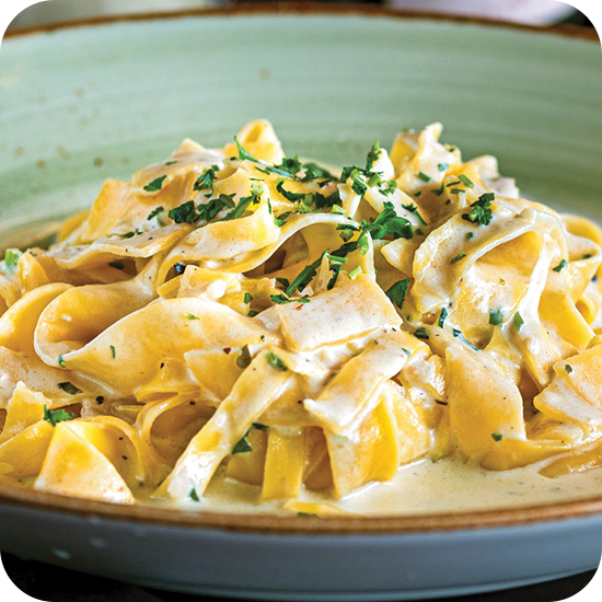 Fettuccine Alfredo pasta in a creamy white sauce, topped with chopped parsley, served in a green bowl.