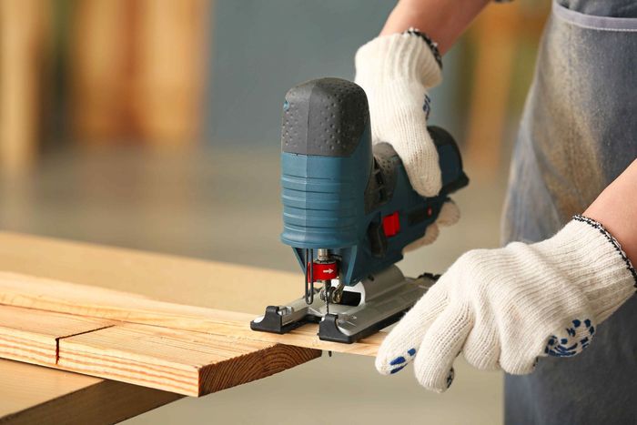 A person is using a jigsaw to cut a piece of wood.