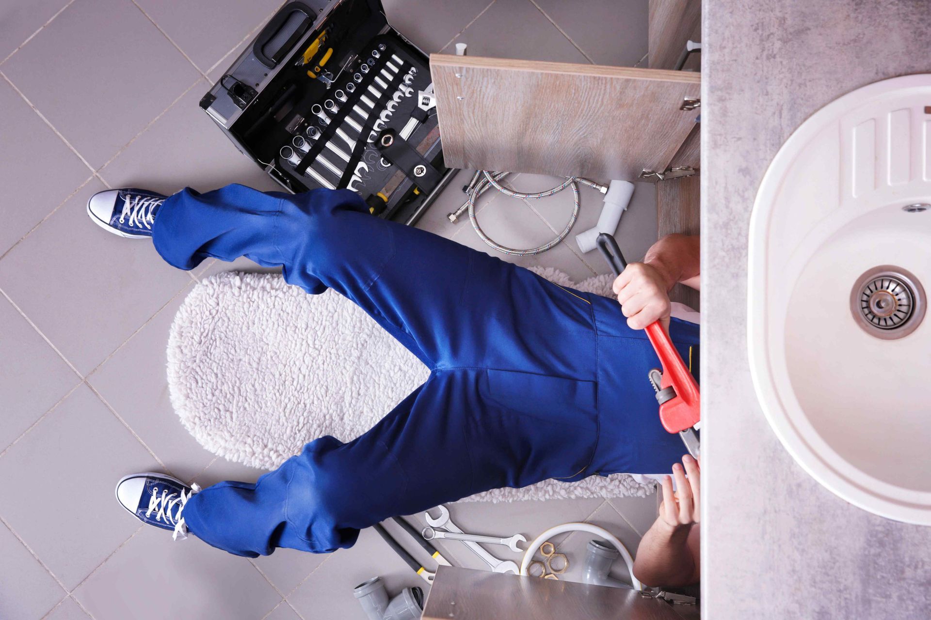 A plumber is laying on the floor working on a sink.