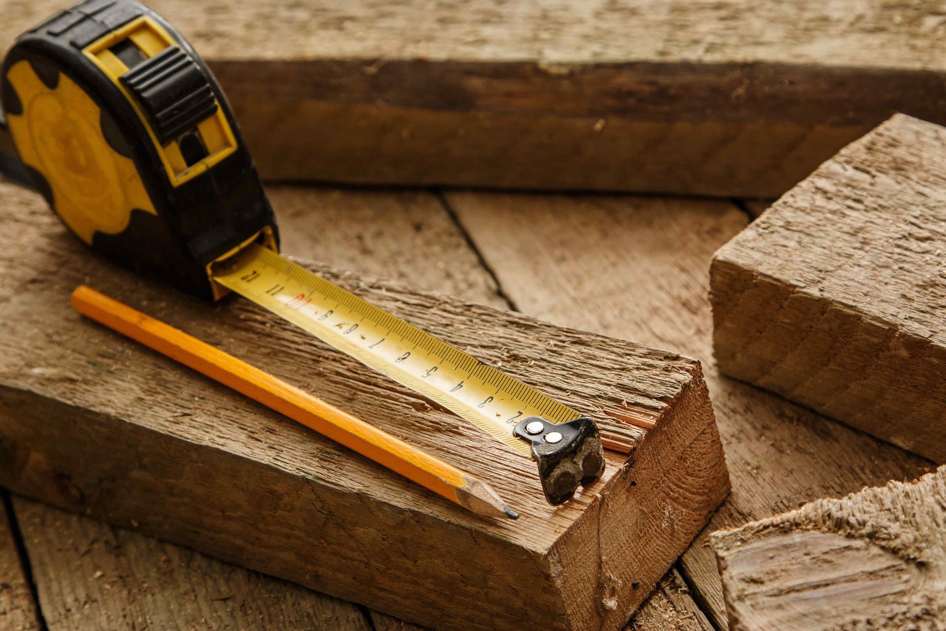 A tape measure and pencil are on a piece of wood.