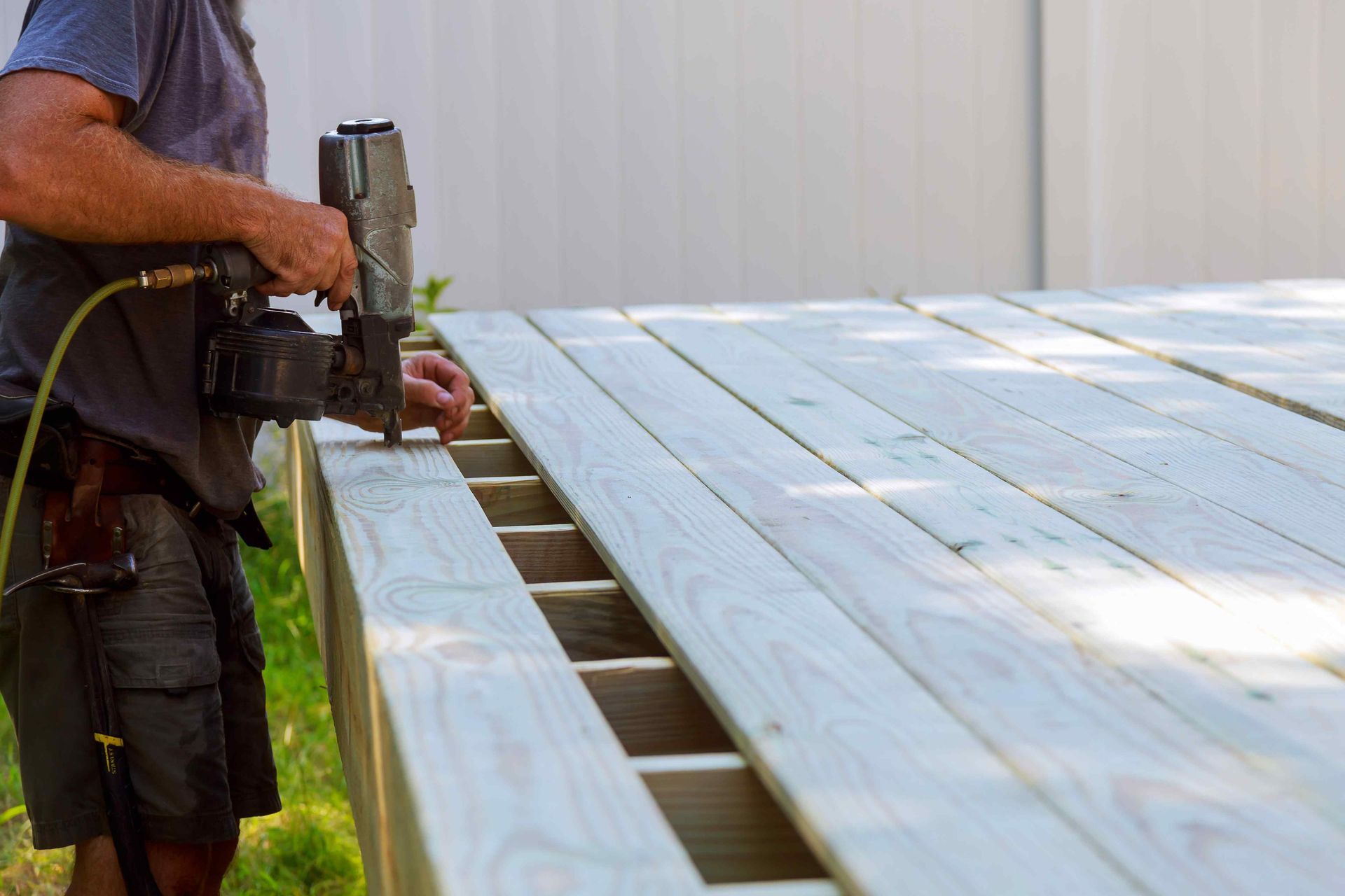 Person using a nail gun to install wooden deck boards.
