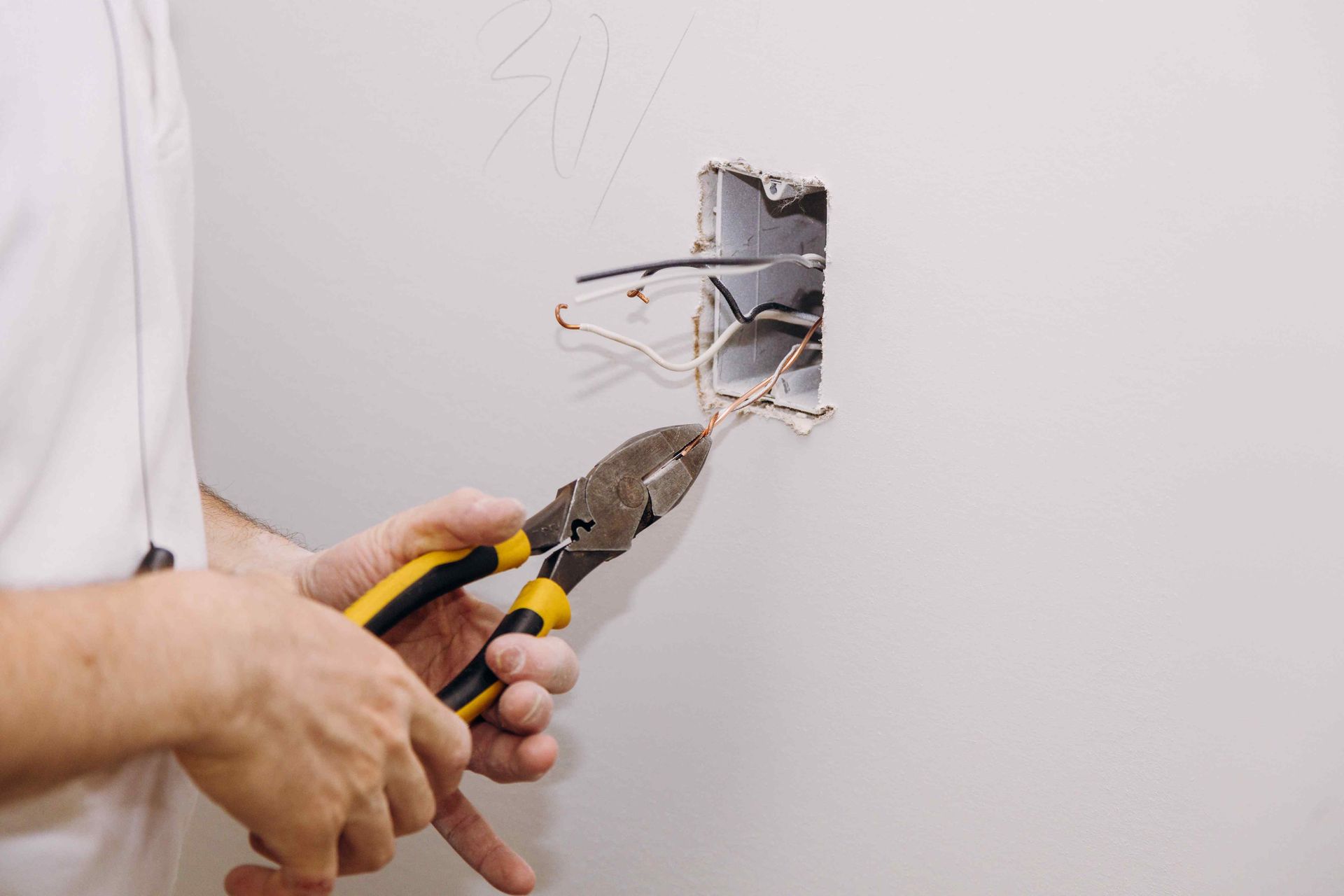 A man is holding a pair of pliers and cutting wires in a wall.