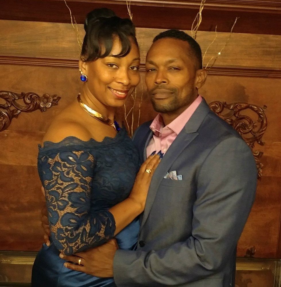 Couple in formal attire; the woman in a blue gown, the man in a suit, both smiling and embracing.