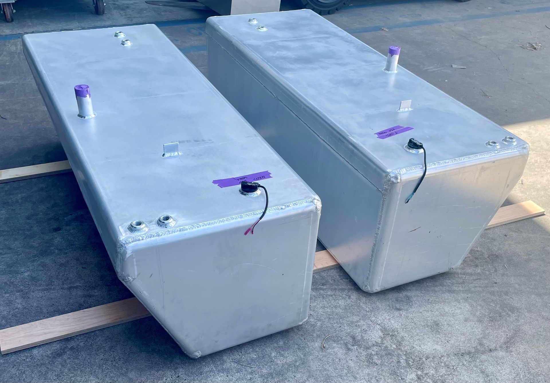 Two large, silver, rectangular metal fuel tanks sitting on wooden supports outside.— Townsville Stainless Steel in Garbutt, QLD