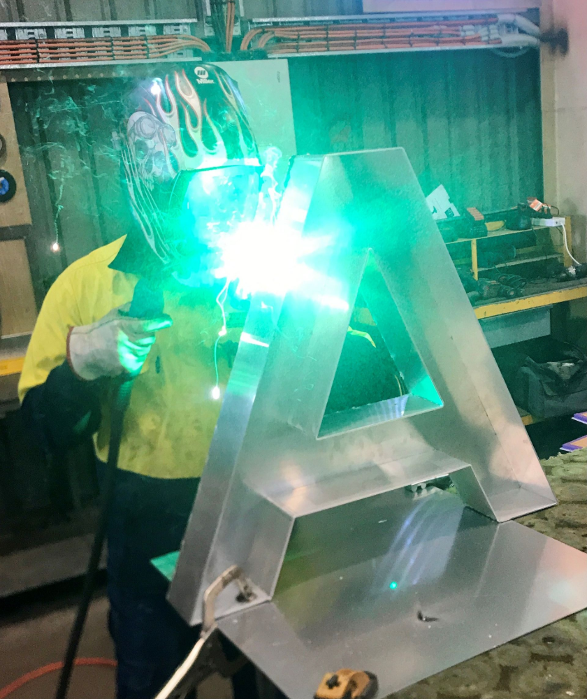 Person welding a large, silver letter