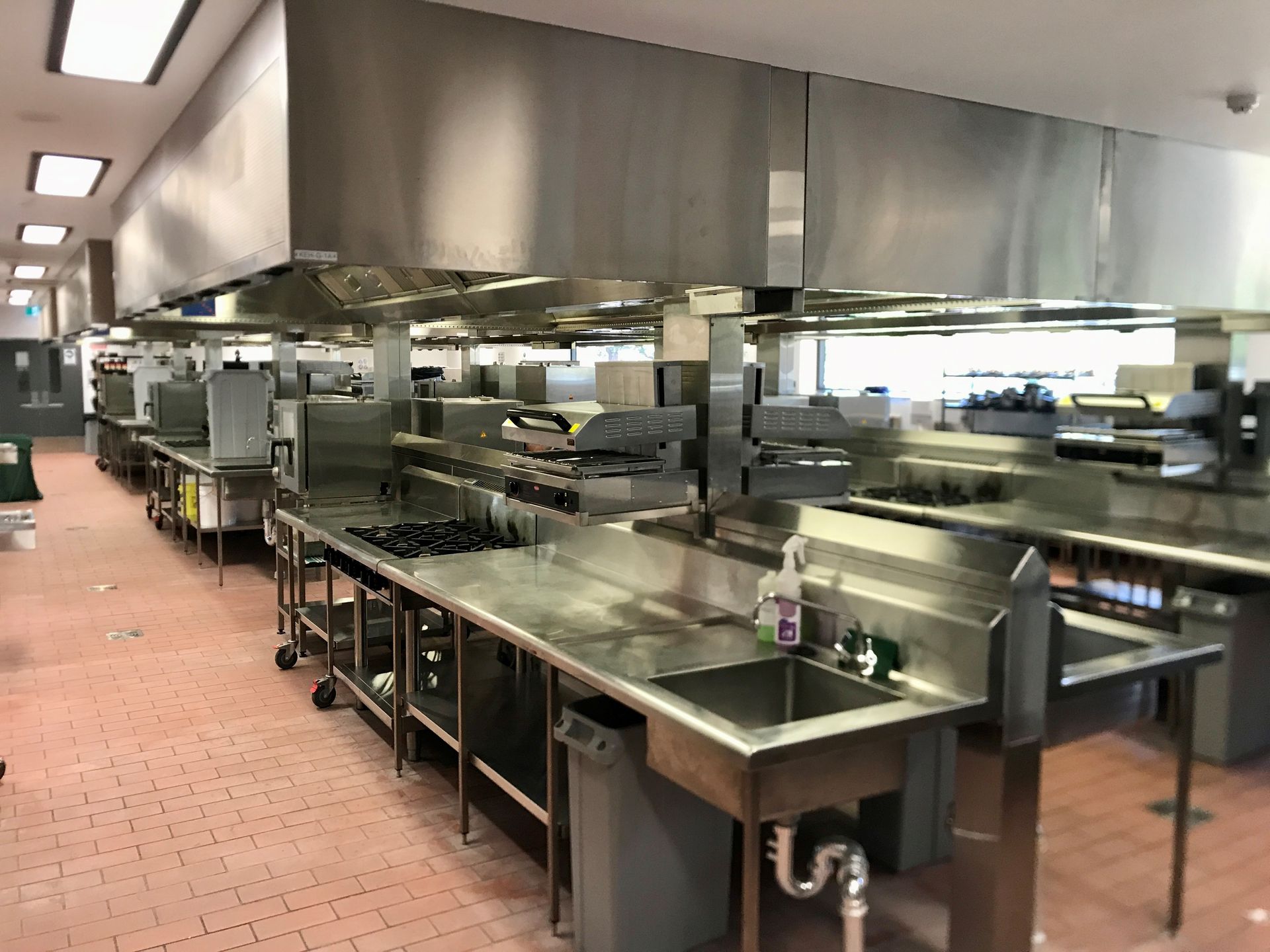 Outdoor kitchen with grills, sink, and storage cabinets under a concrete overhang.— Townsville Stainless Steel in Garbutt, QLD