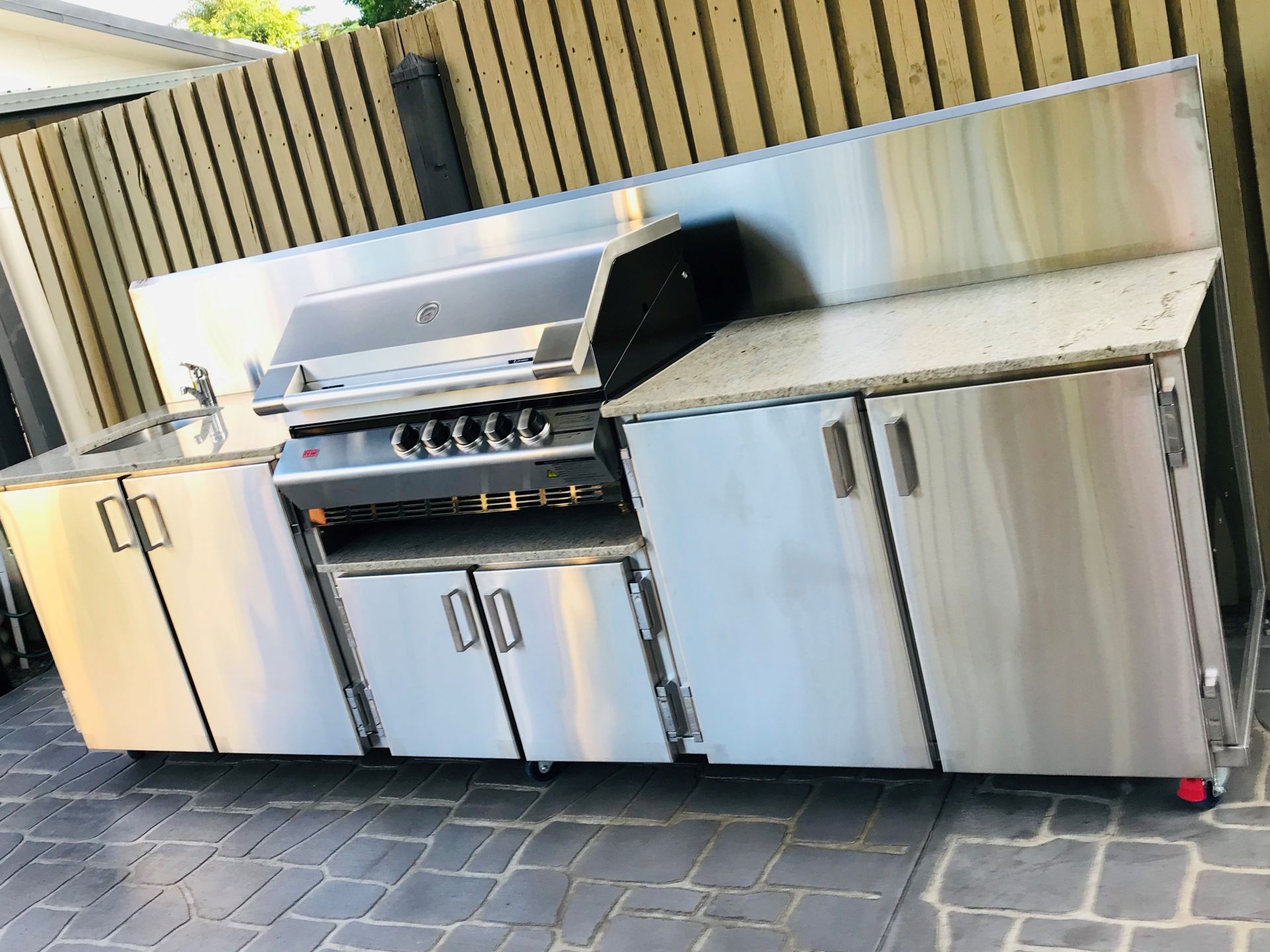 Outdoor stainless steel kitchen with grill, cabinets, countertop, sink, and wood fence backdrop — Townsville Stainless Steel in Garbutt, QLD