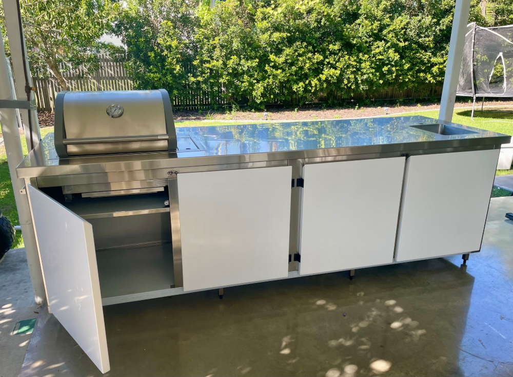 Outdoor stainless steel BBQ with white cabinet doors on a concrete patio.— Townsville Stainless Steel in Garbutt, QLD