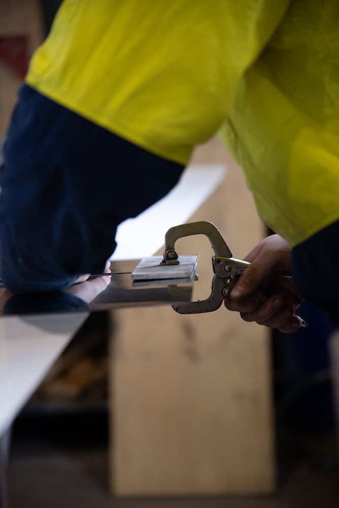 A Person in a Yellow Shirt is Holding a Clamp on a Piece of Metal— Townsville Stainless Steel in Garbutt, QLD