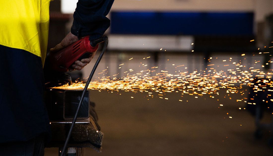 A Man Is Using a Grinder to Cut a Piece of Metal — Townsville Stainless Steel in Garbutt, QLD