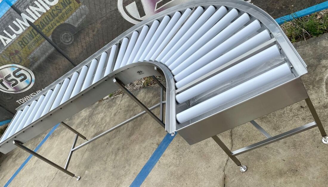 A Stainless Steel Conveyor Belt with White Rollers Is Sitting on The Ground — Townsville Stainless Steel in Garbutt, QLD