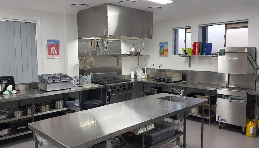 A Large Kitchen with Stainless Steel Appliances and A Large Table — Townsville Stainless Steel in Garbutt, QLD