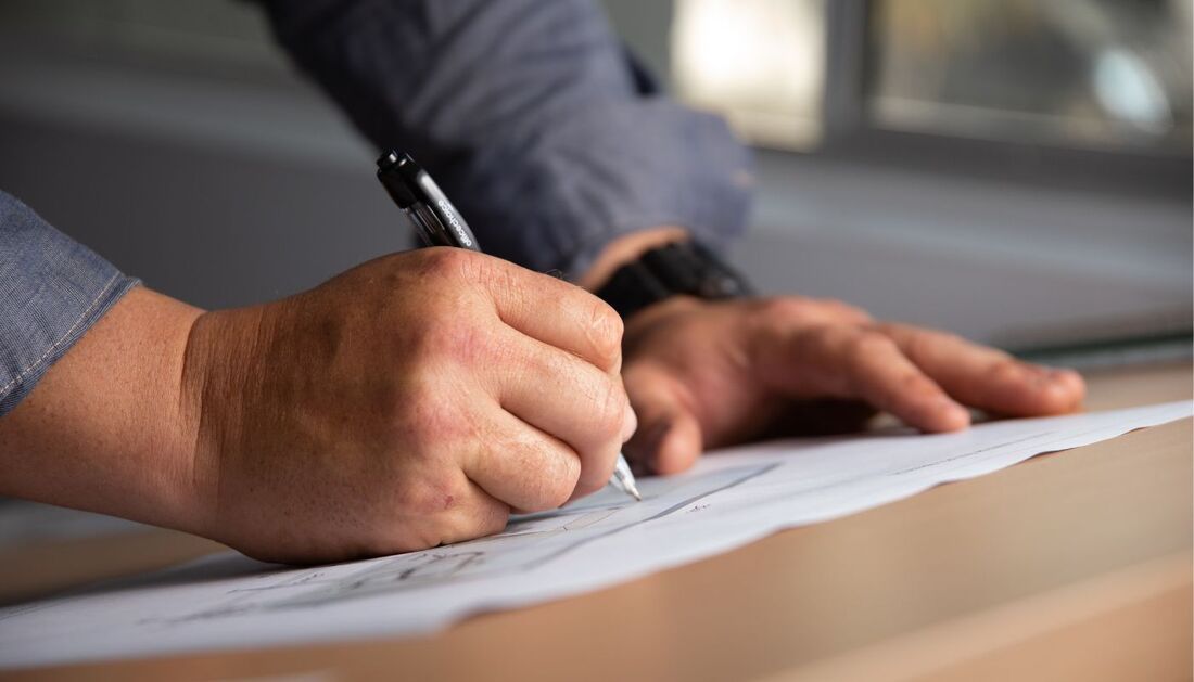 A Man Is Writing on A Piece of Paper with A Pen — Townsville Stainless Steel in Garbutt, QLD