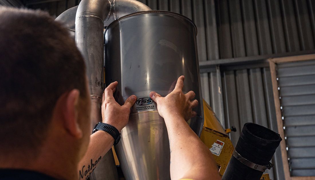 A Man Is Working on A Metal Pipe in A Factory — Townsville Stainless Steel in Garbutt, QLD