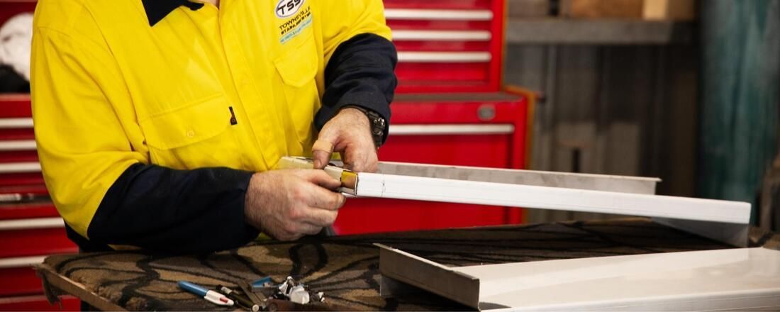 A Man in A Yellow Shirt Is Cutting a Piece of Metal with A Pair of Scissors — Townsville Stainless Steel in Garbutt, QLD