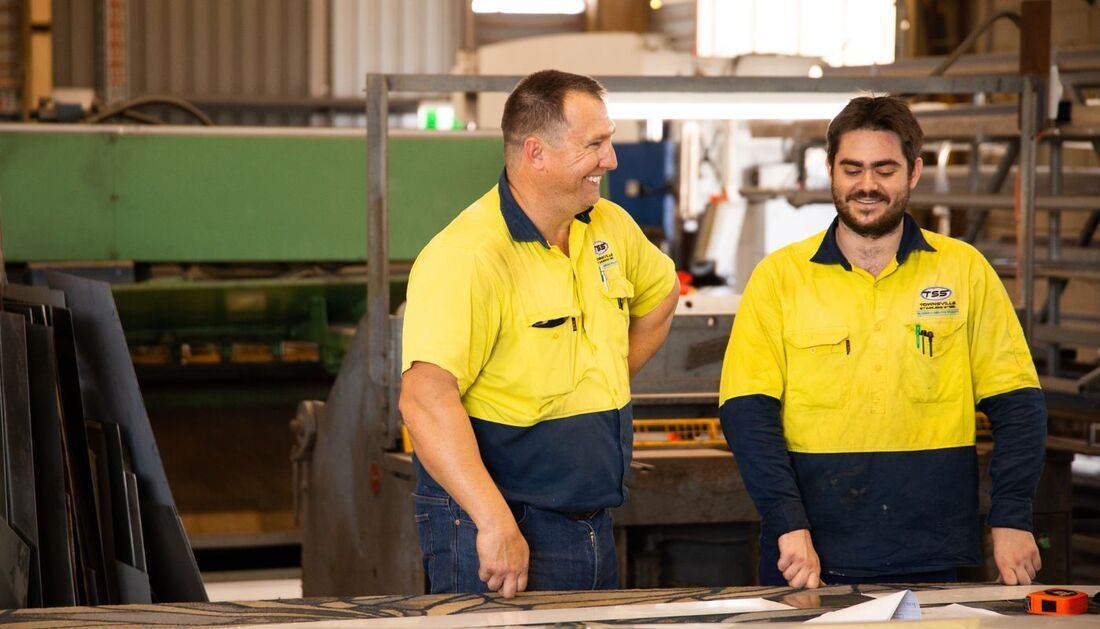Two Men Are Standing Next to Each Other in A Factory Talking to Each Other — Townsville Stainless Steel in Garbutt, QLD