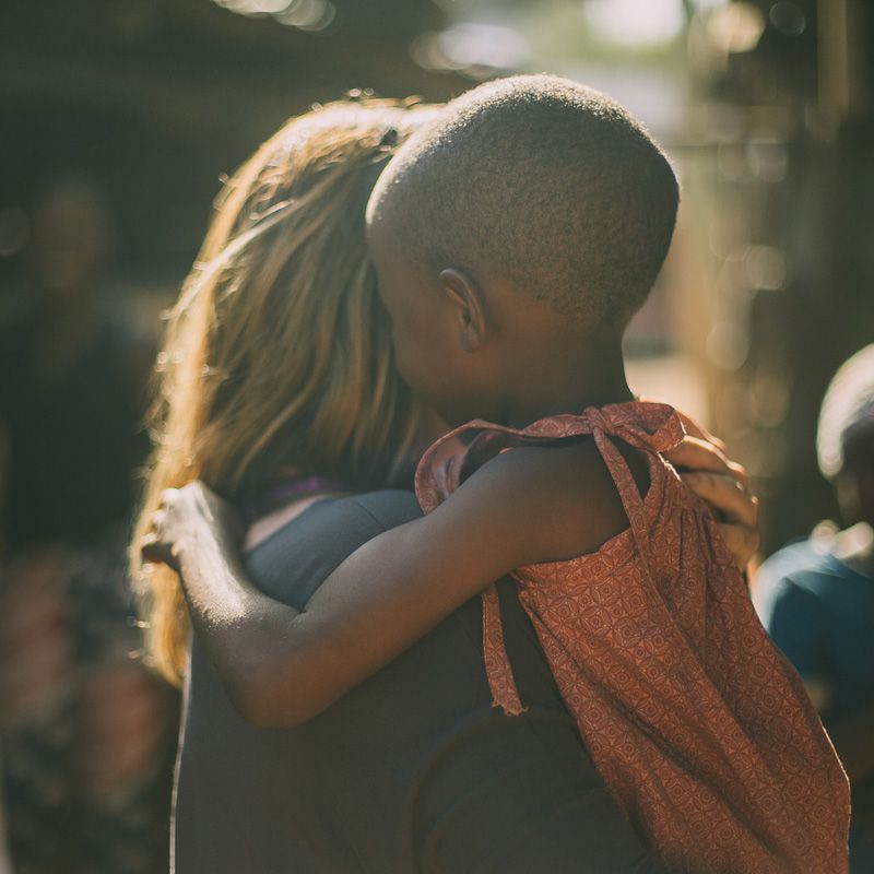 A woman is hugging a child who is wearing a pink dress.