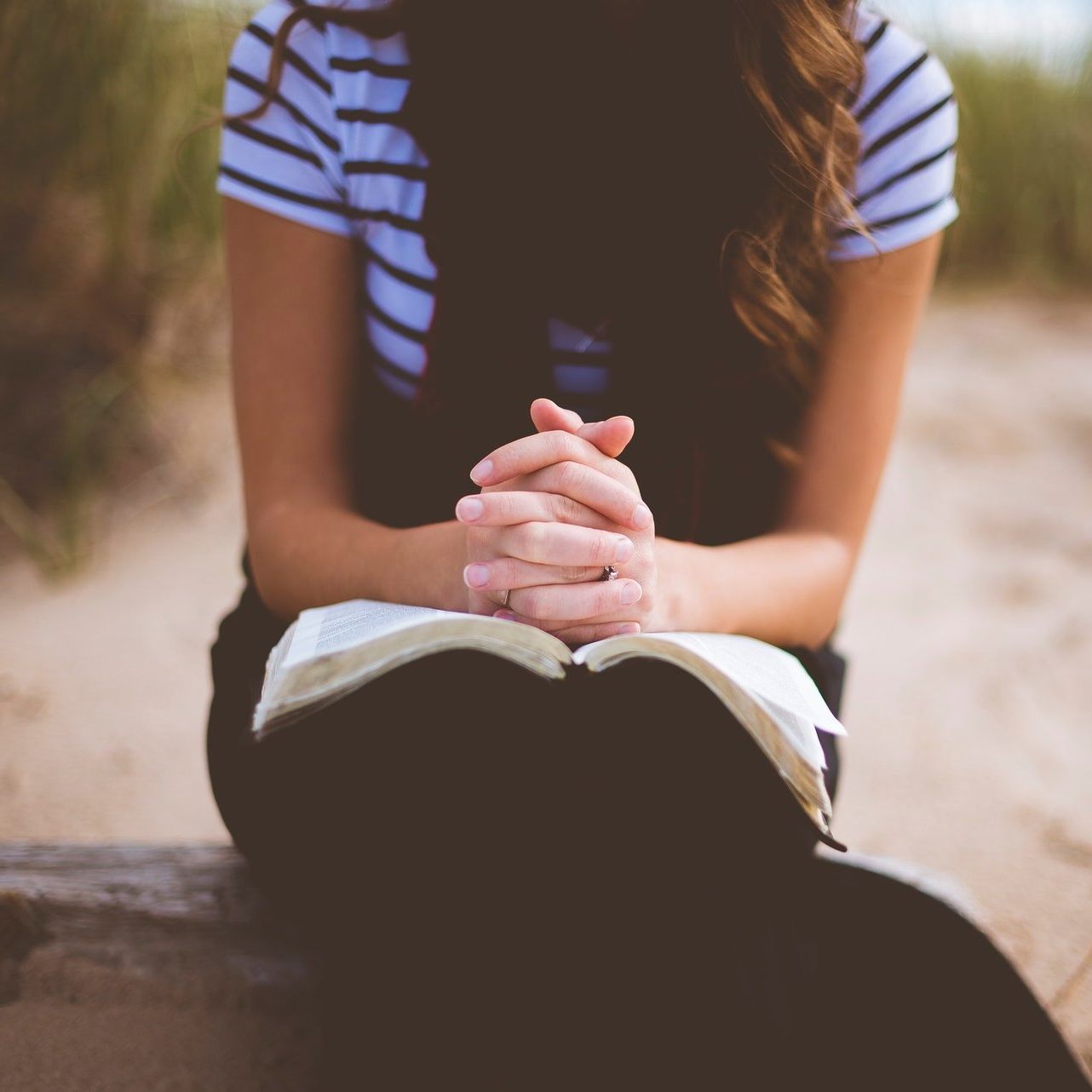 A woman is sitting with her hands folded over a bible.