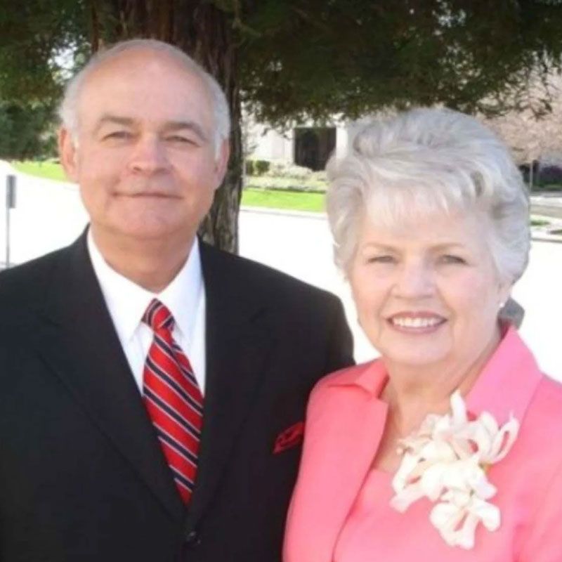 A man in a suit and tie stands next to a woman in a pink jacket