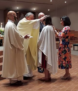 A religious ceremony in a church; a priest blesses a woman draped in a white cloth.