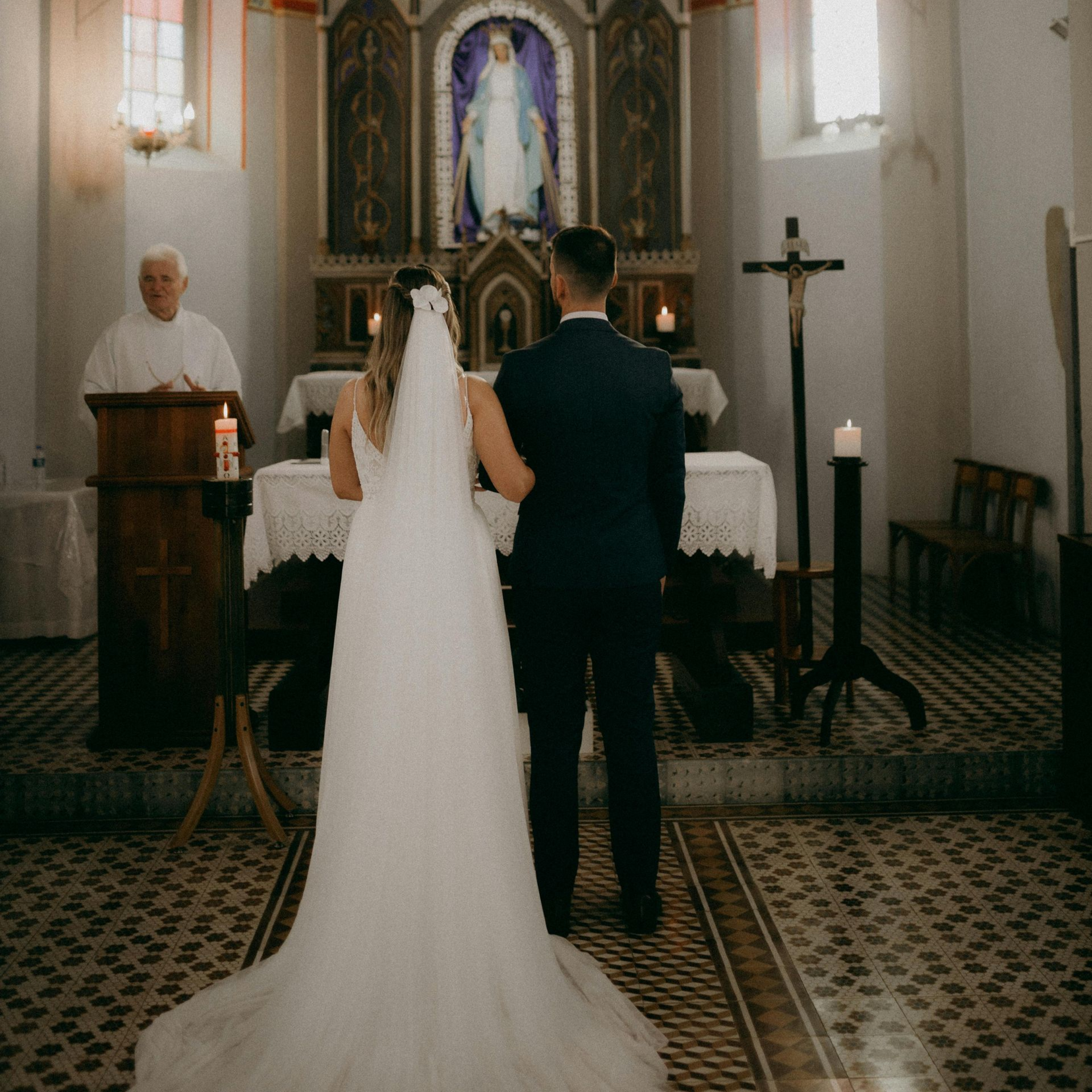 A bride and groom stand hand in hand at the altar in a church. 