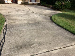 A concrete driveway leading to a house with a hose attached to it.