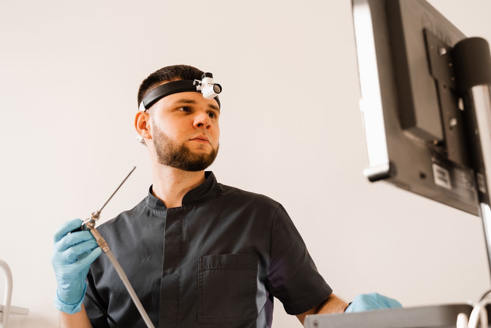 A man is holding a surgical instrument in front of a computer monitor.