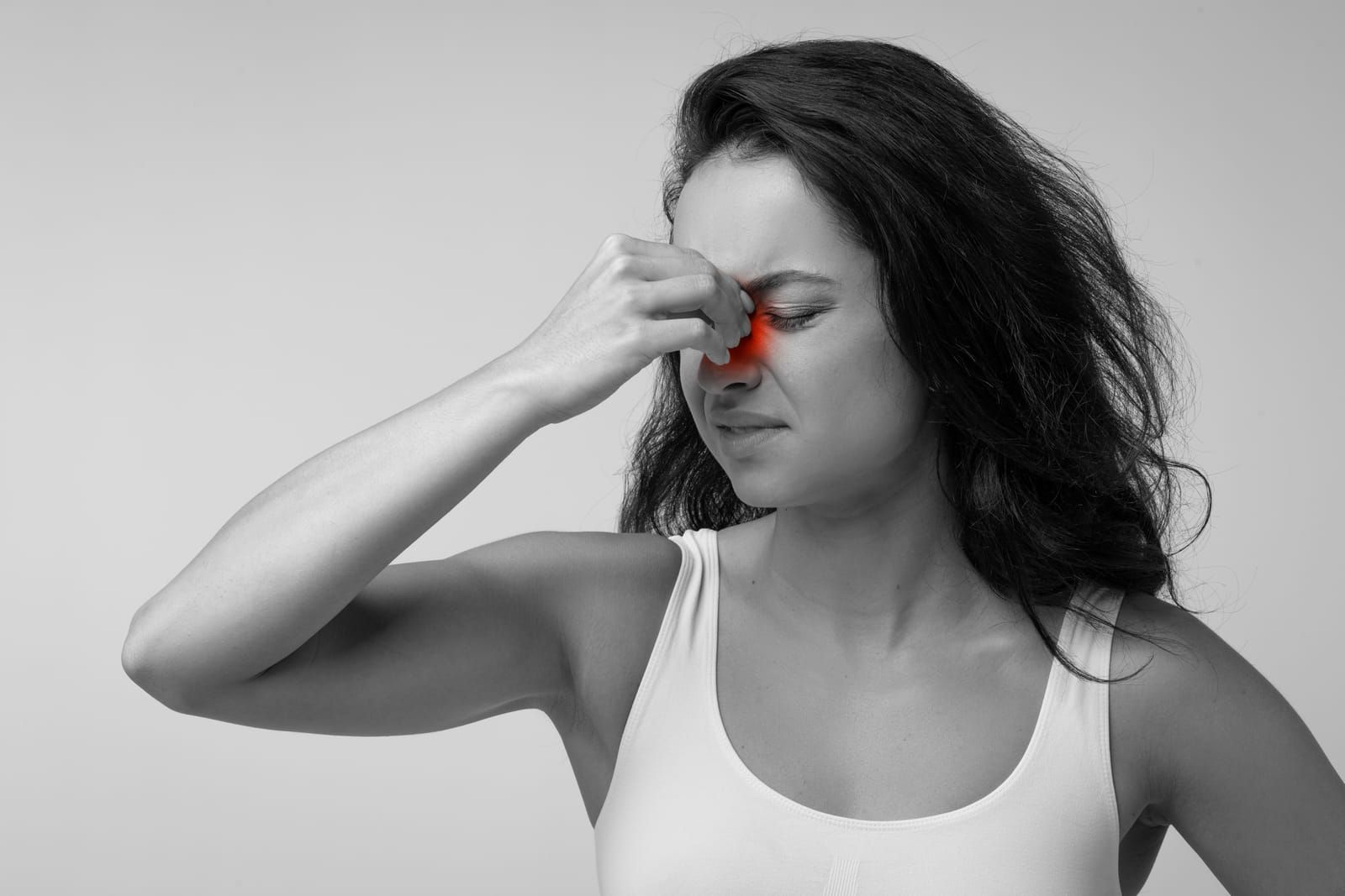A woman is holding her nose because she has a sinus headache.