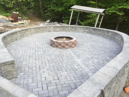 Outdoor kitchen with grill, cooktop, and refrigerator; surrounded by trees and greenery.