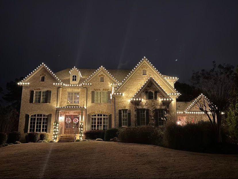 A residential home at night decorated with numerous glowing Christmas lights, icicle lights, and a white picket fence.