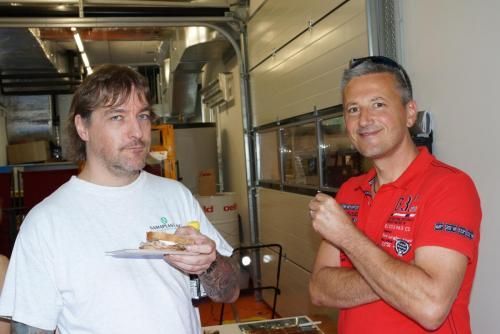 Zwei Männer stehen nebeneinander und einer hält einen Teller mit Essen.