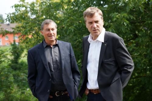 Zwei Männer in Anzügen stehen mit den Händen in den Taschen nebeneinander.