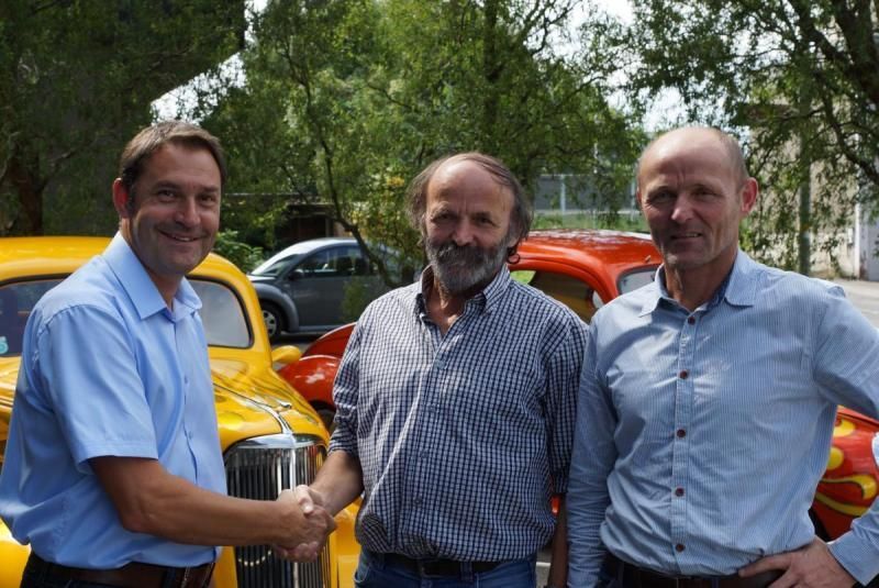 Drei Männer schütteln sich vor einem gelben Auto die Hände