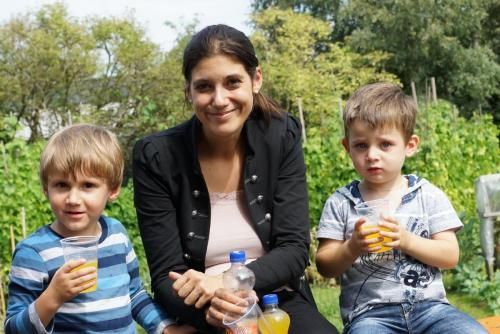 Eine Frau sitzt neben zwei kleinen Jungen und trinkt Orangensaft.