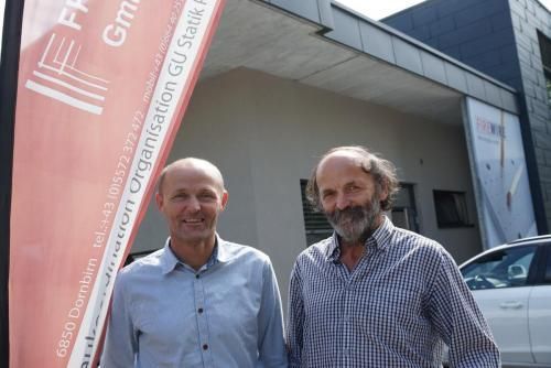 Zwei Männer stehen nebeneinander vor einem Gebäude.