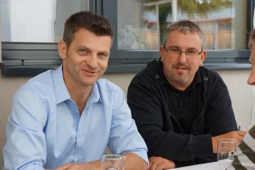 Zwei Männer sitzen mit Weingläsern an einem Tisch.
