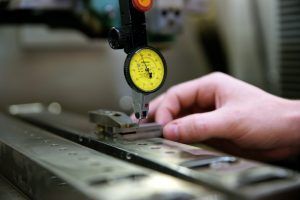 Eine Person misst ein Stück Metall mit einer Messuhr.