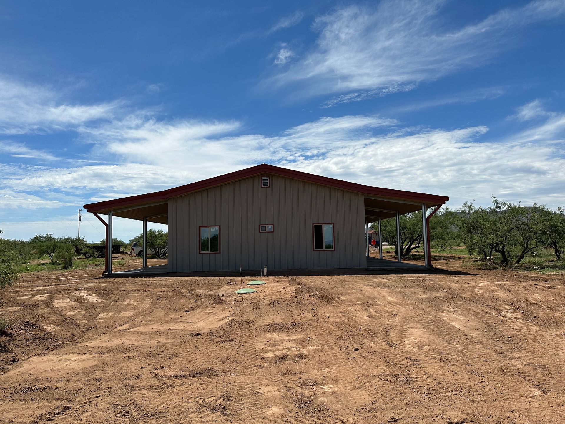A small house with a porch is sitting in the middle of a dirt field.