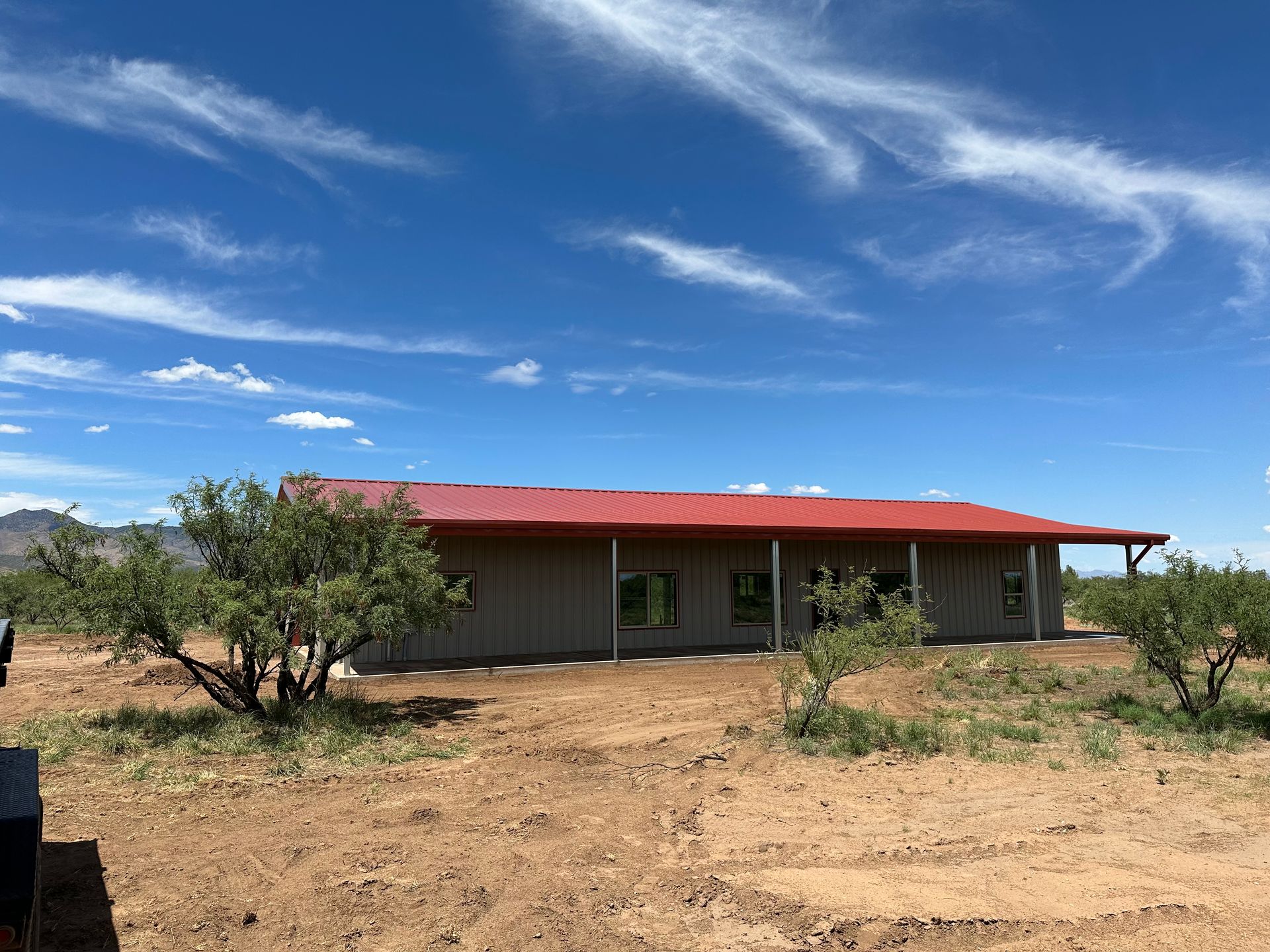 A large house with a red roof is sitting in the middle of a dirt field.