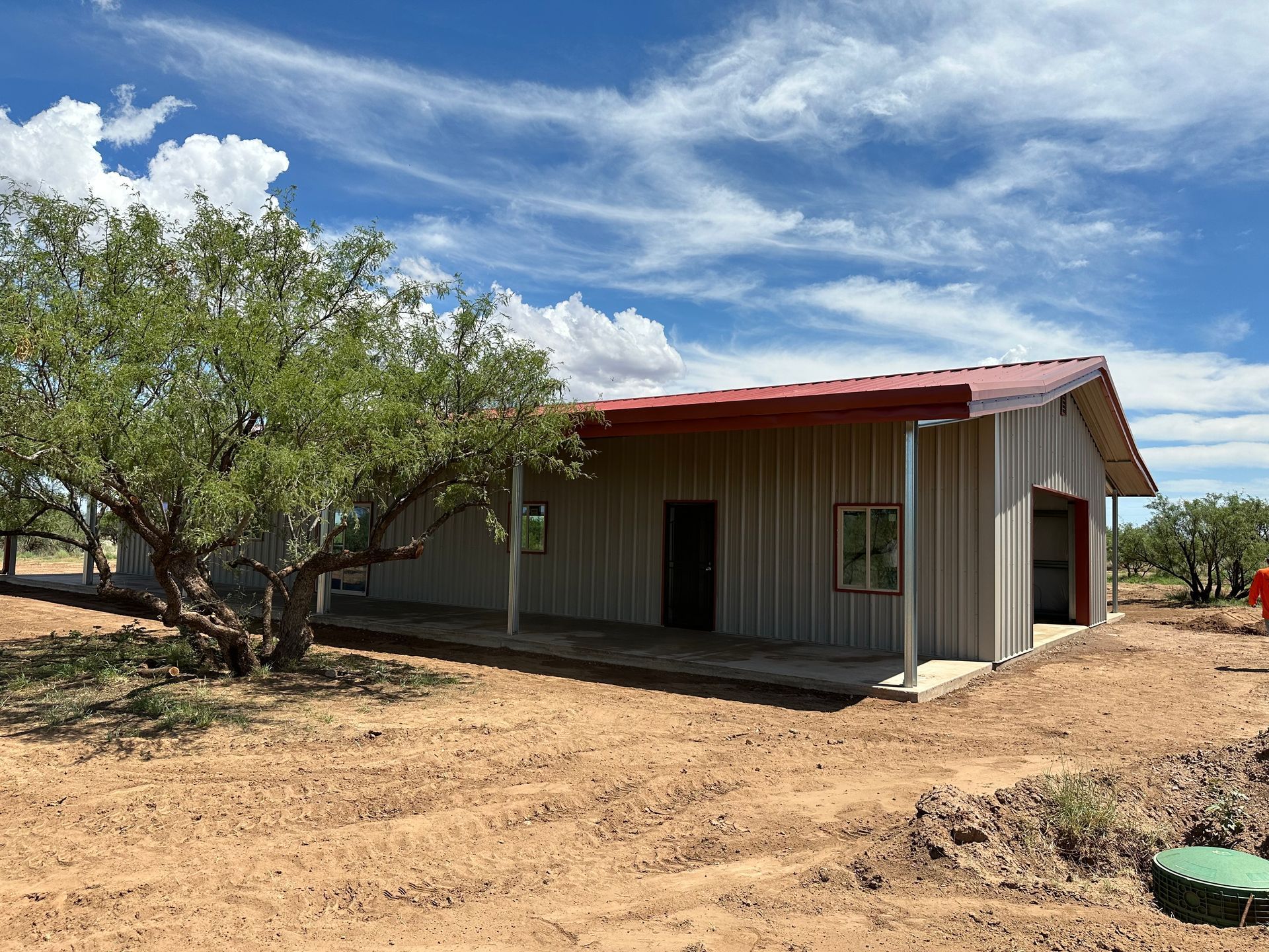 A house with a red roof is sitting in the middle of a dirt field.
