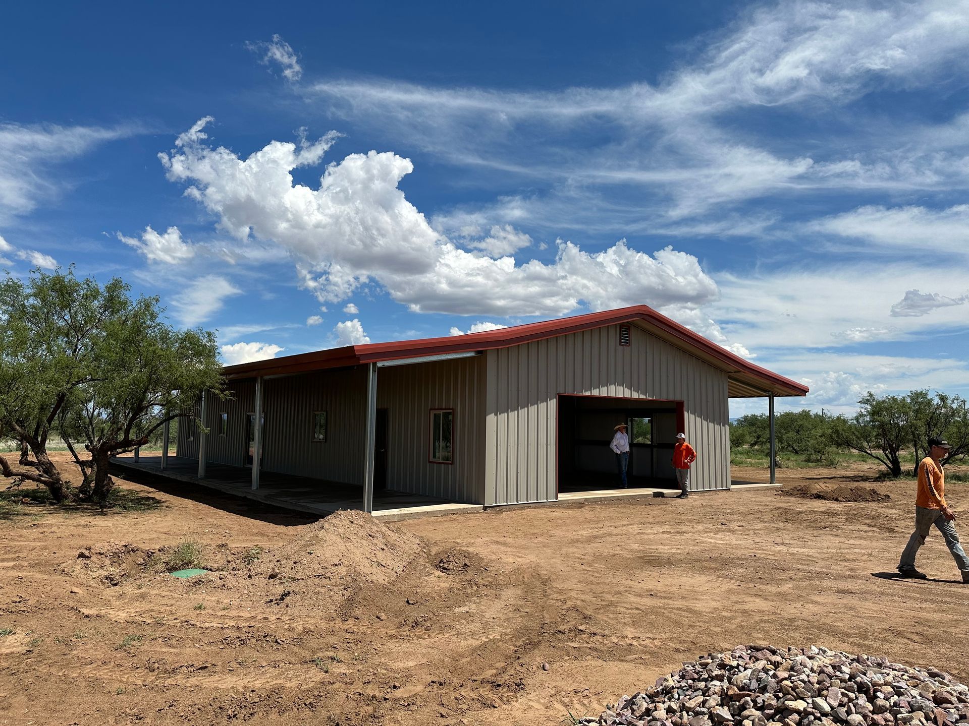 A man is standing in front of a building in the middle of a dirt field.