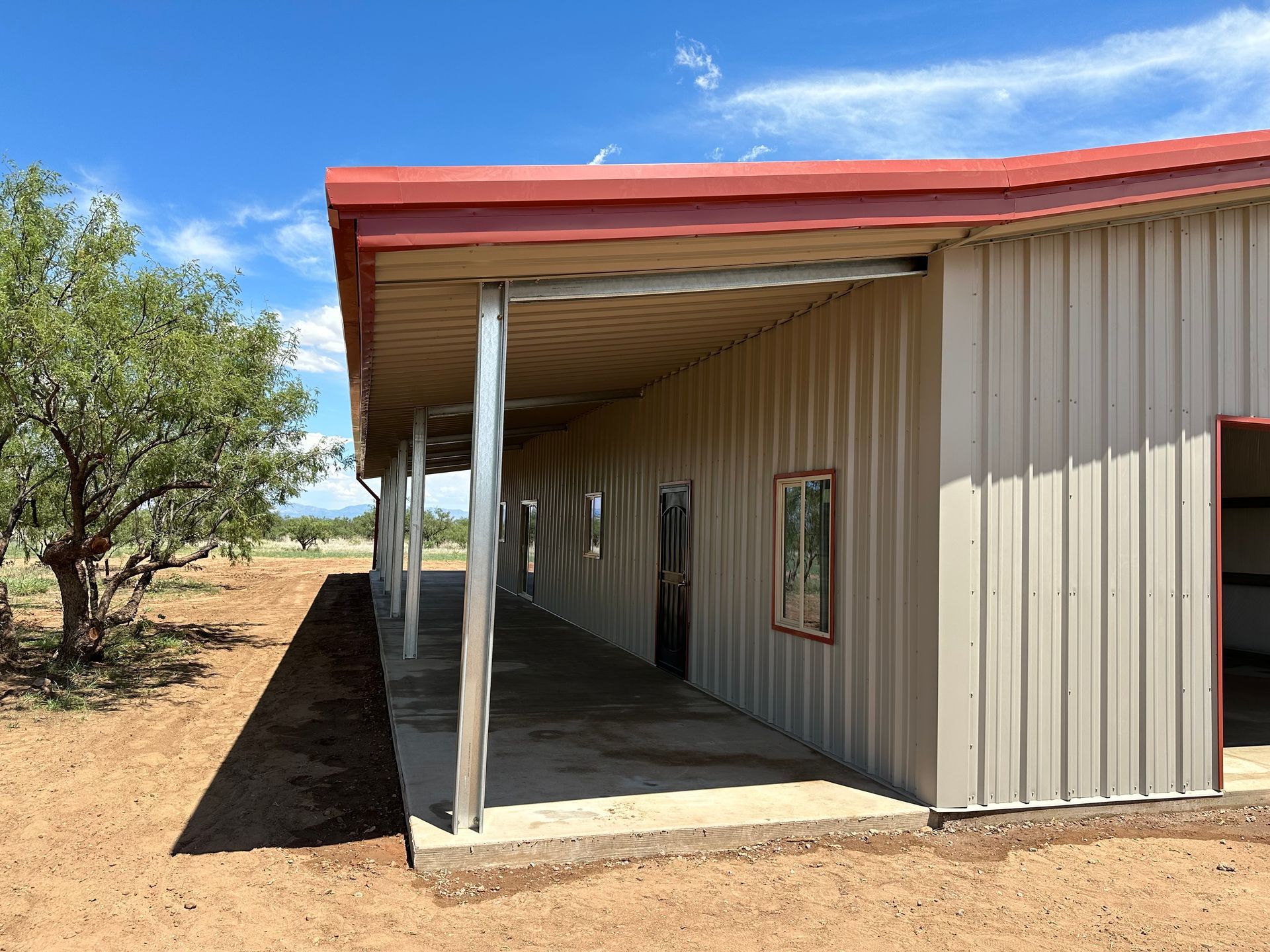 A large metal building with a red roof and a porch.